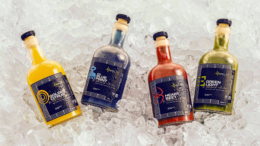 Four bottles of juice with clear labels, displayed in a row, with ice cubes in front of them.